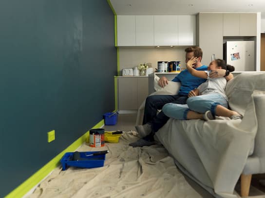 A couple in their rental apartment sitting on a couch resting after painting their lounge room wall